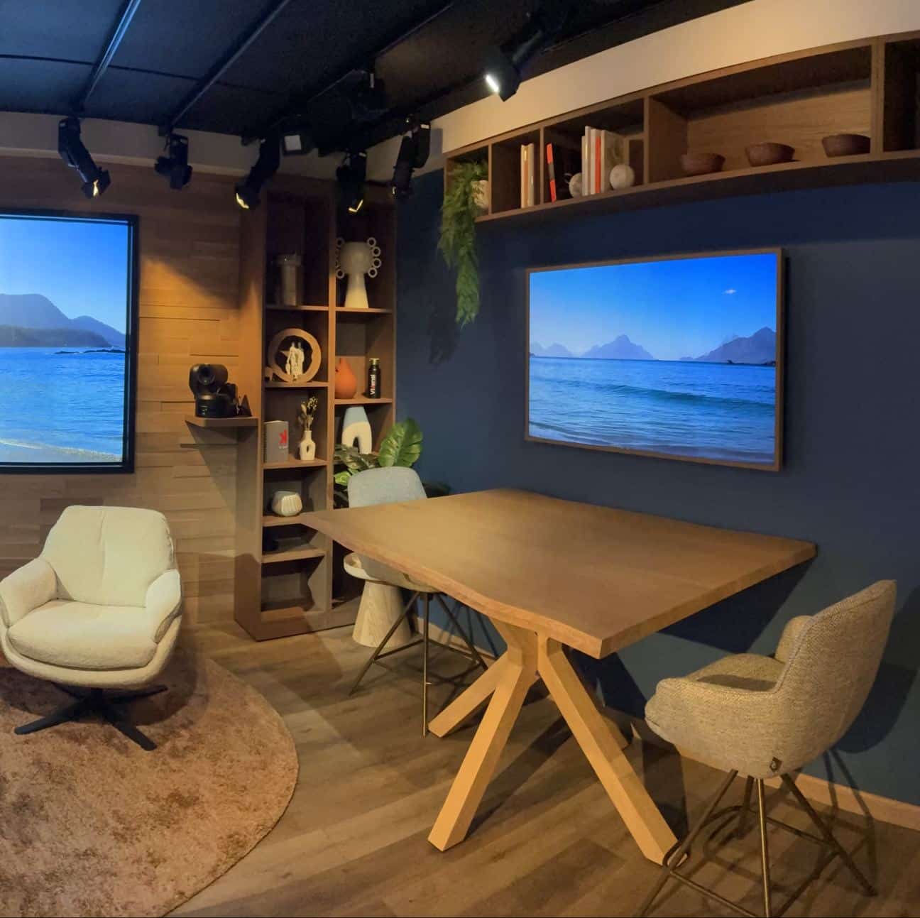 Plateau du studio : fauteuil, table en bois, écrans et bibliothèque