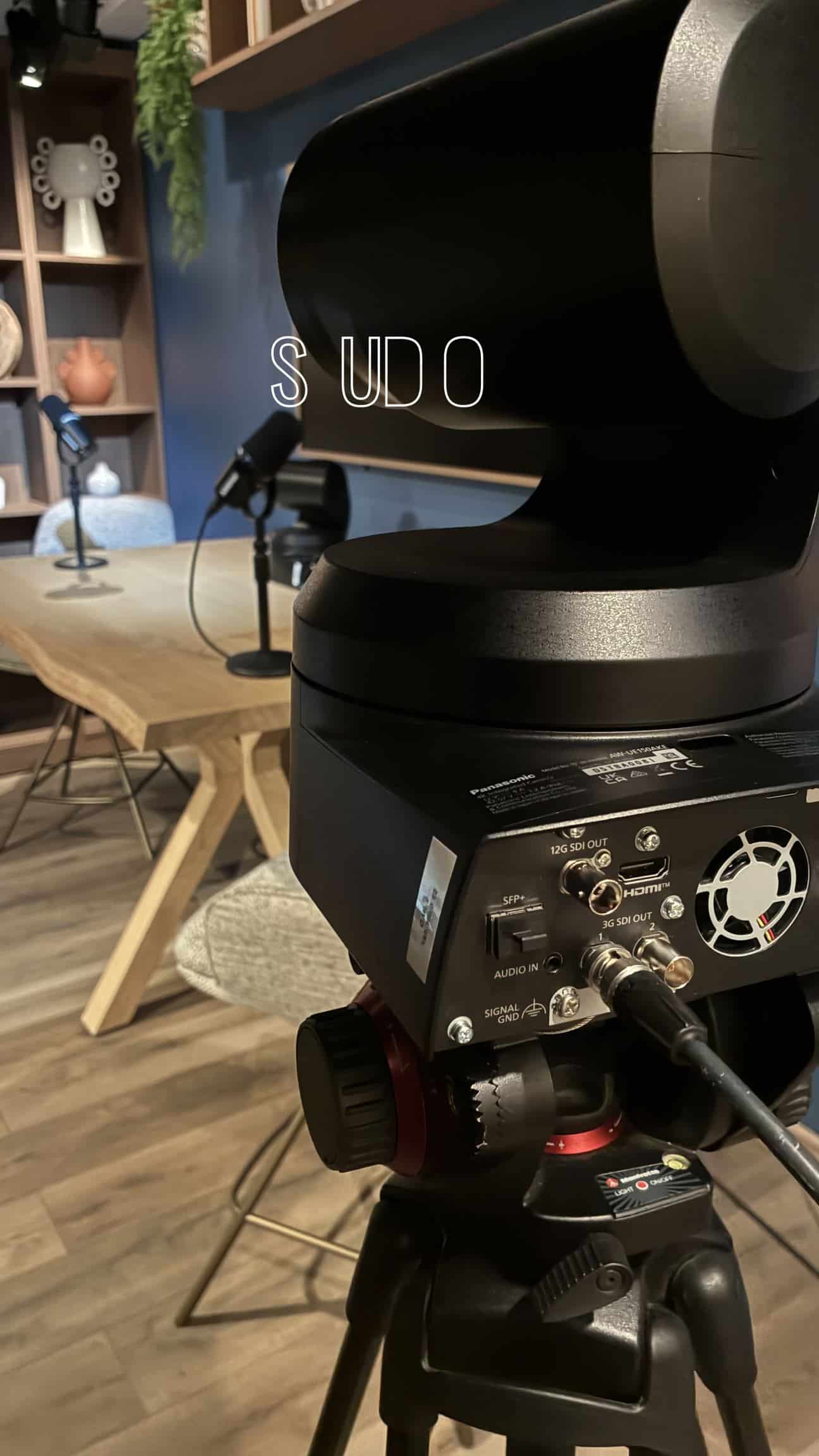 Caméra robotisée Panasonic sur trépied, table et micros du studio